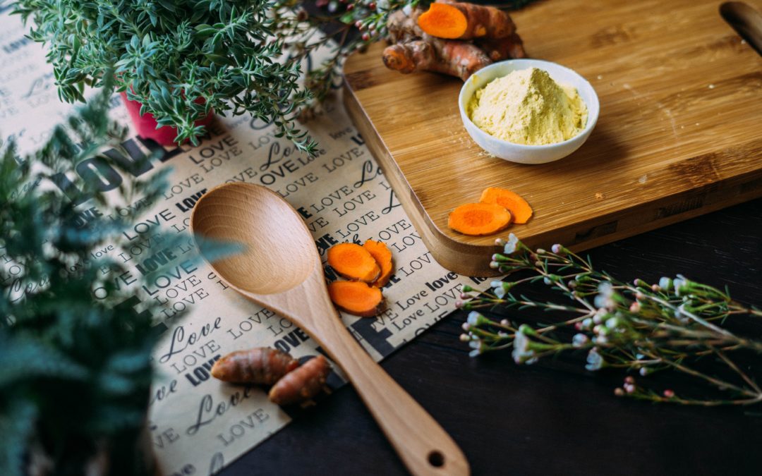 Sliced fresh turmeric and ground turmeric on a wooden cutting board with a wooden spoon and plants beside it