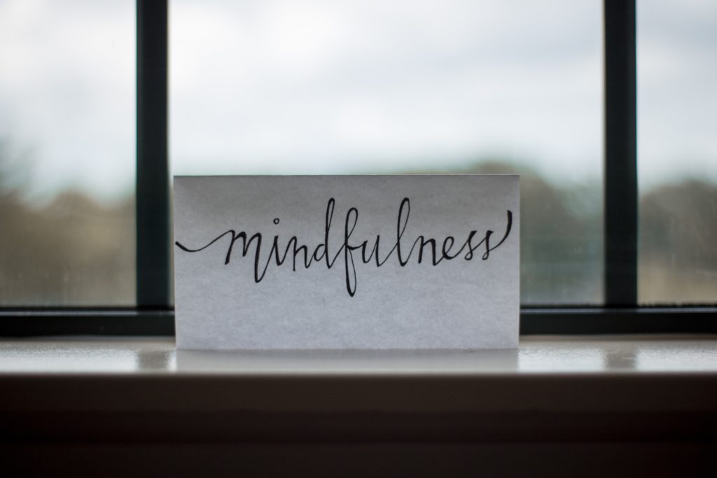 a paper that reads “mindfulness” in cursive font sitting on a window ledge