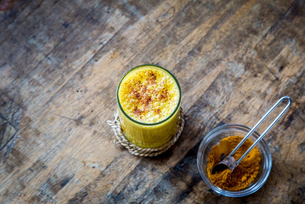 A glass of a bright yellow turmeric beverage with a container of ground turmeric beside it