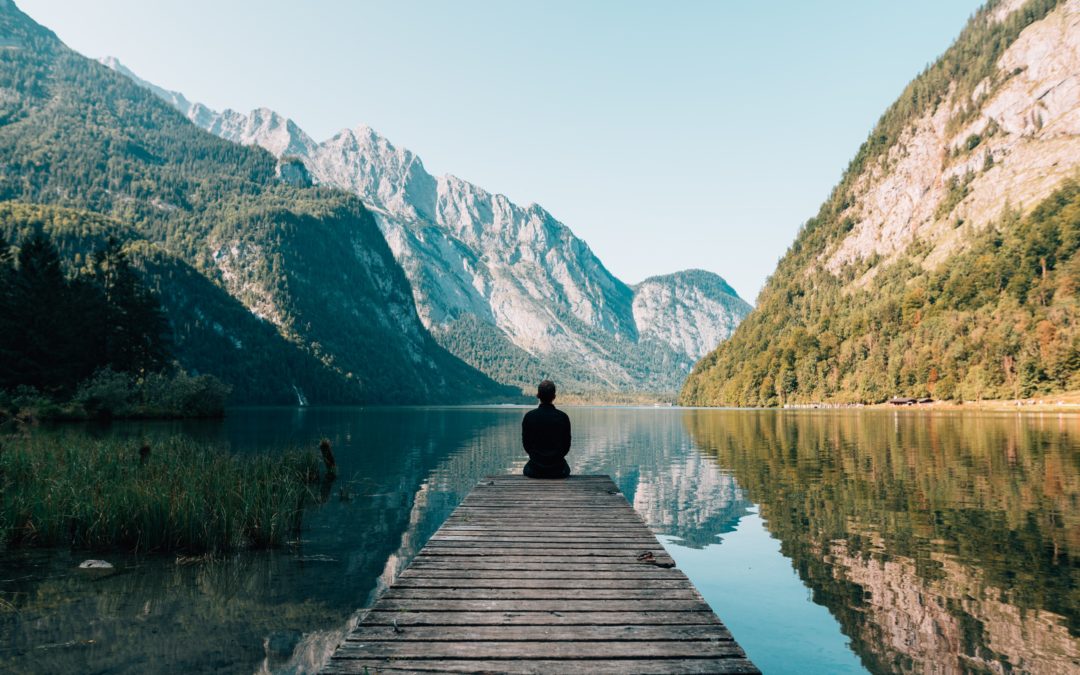 Person sitting at the end of a dock over the water looking at mountains